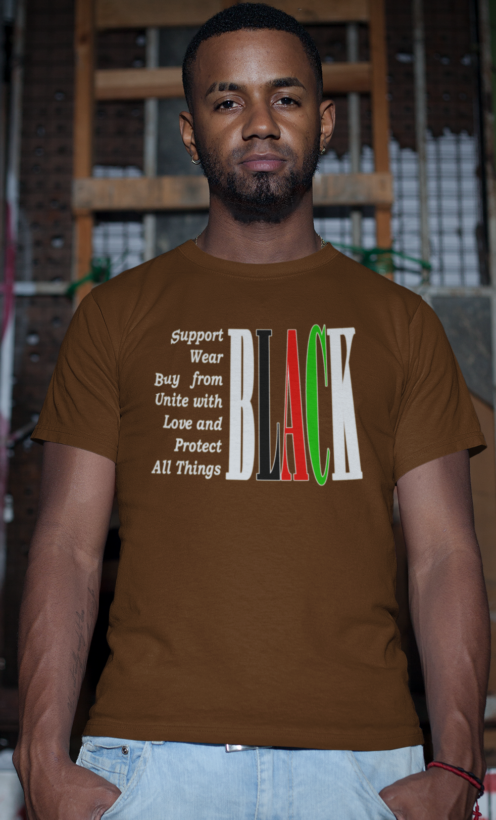 Man wearing a brown t-shirt with text and colorful design, standing against a graffiti-covered wall.