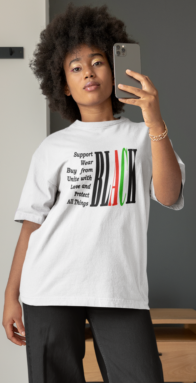 Person taking a mirror selfie wearing a white t-shirt with a graphic design in a bedroom.
