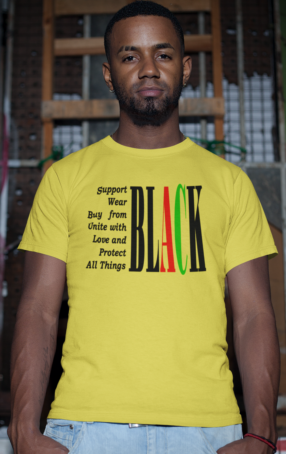 Man wearing a yellow t-shirt with text and colors, standing against a graffiti-covered wall.