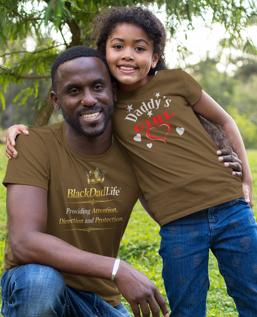 Man and child wearing matching brown t-shirts in a grassy outdoor setting