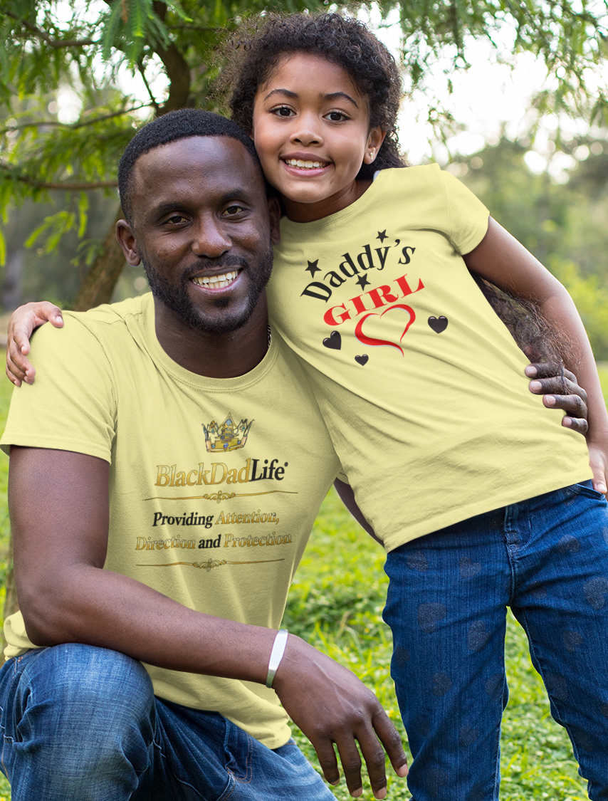 Man and young girl wearing matching yellow t-shirts in a grassy outdoor setting