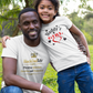Man and young girl posing together in a grassy field wearing matching 'Daddy's Girl' t-shirts.