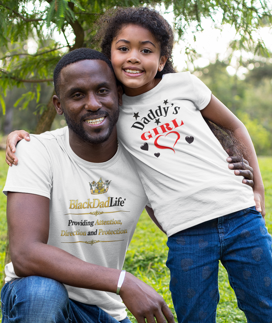 Man and young girl posing together in a grassy field wearing matching 'Daddy's Girl' t-shirts.