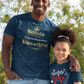 Man and young girl wearing matching navy blue t-shirts outdoors with trees in the background