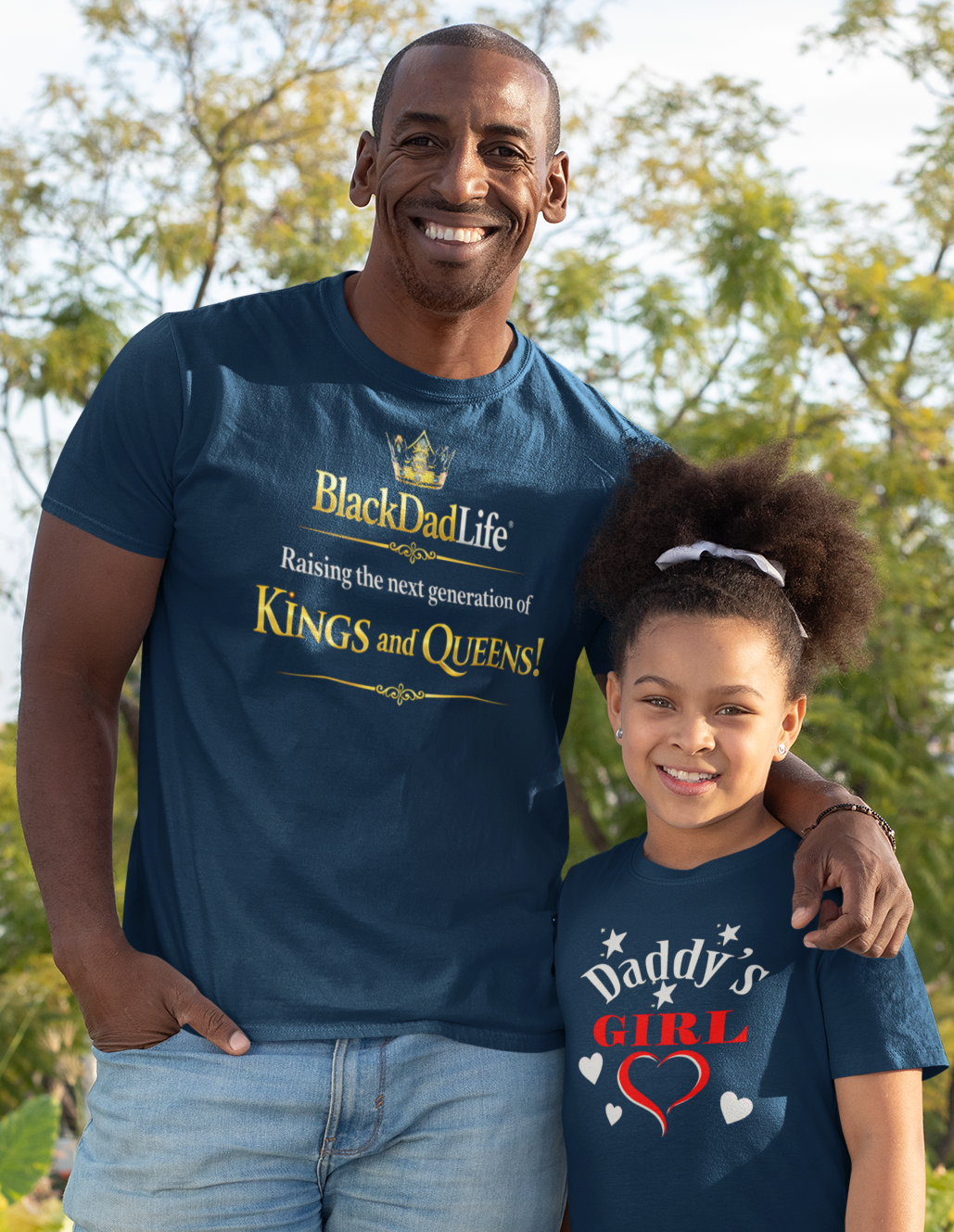 Man and young girl wearing matching navy blue t-shirts outdoors with trees in the background