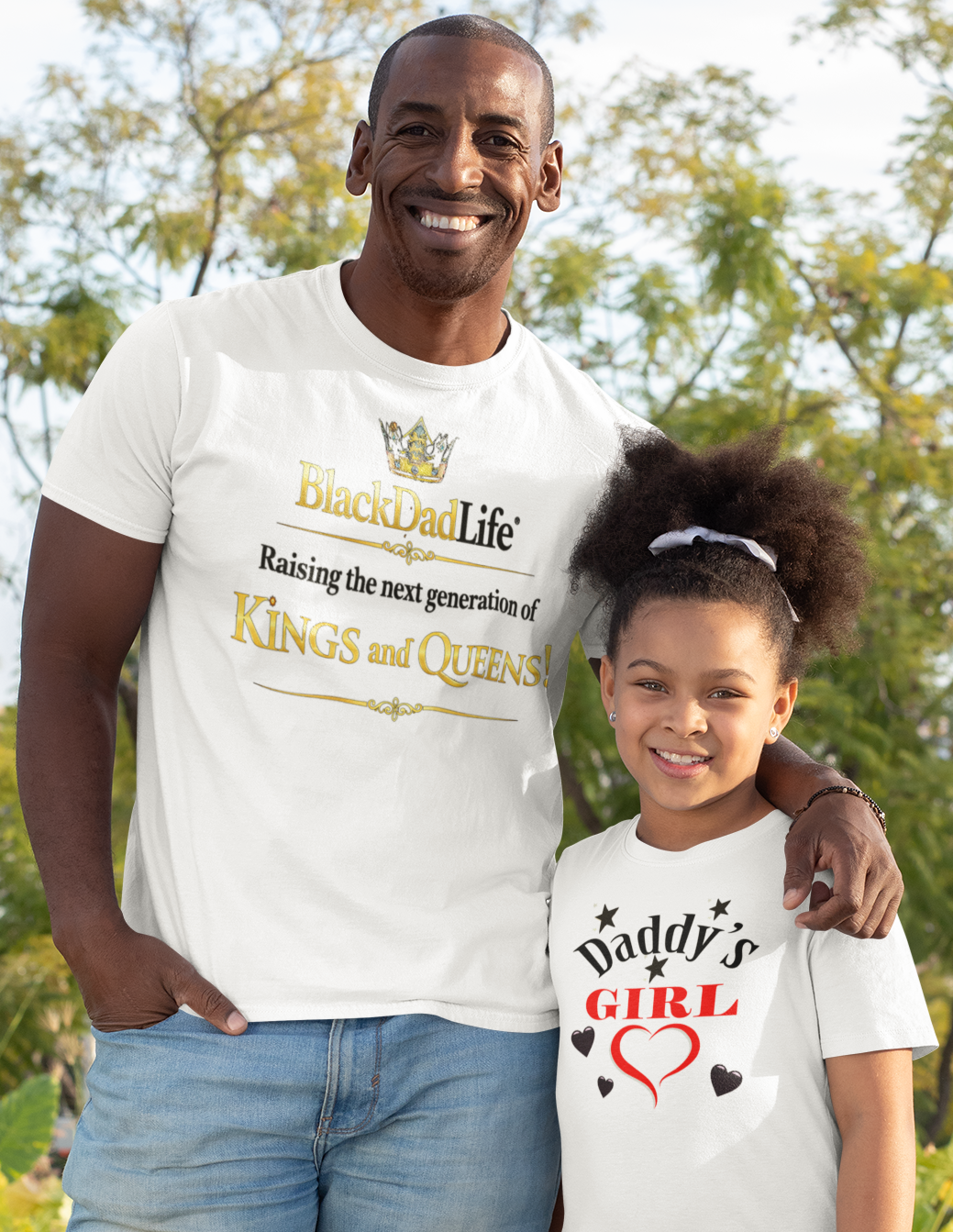 Man and young girl standing outdoors wearing matching white t-shirts with text.