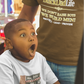 Child in a toy store with a surprised expression, wearing a 'Big Boy' t-shirt.
