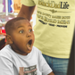 Child in a toy store with a surprised expression, wearing a 'Big Boy' t-shirt.