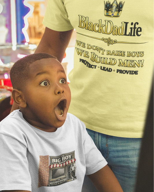Child in a toy store with a surprised expression, wearing a 'Big Boy' t-shirt.
