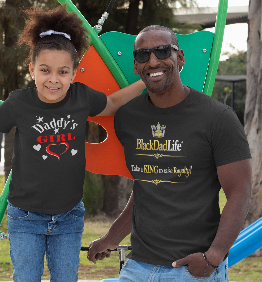 Man and young girl wearing matching black t-shirts with text, standing outdoors.