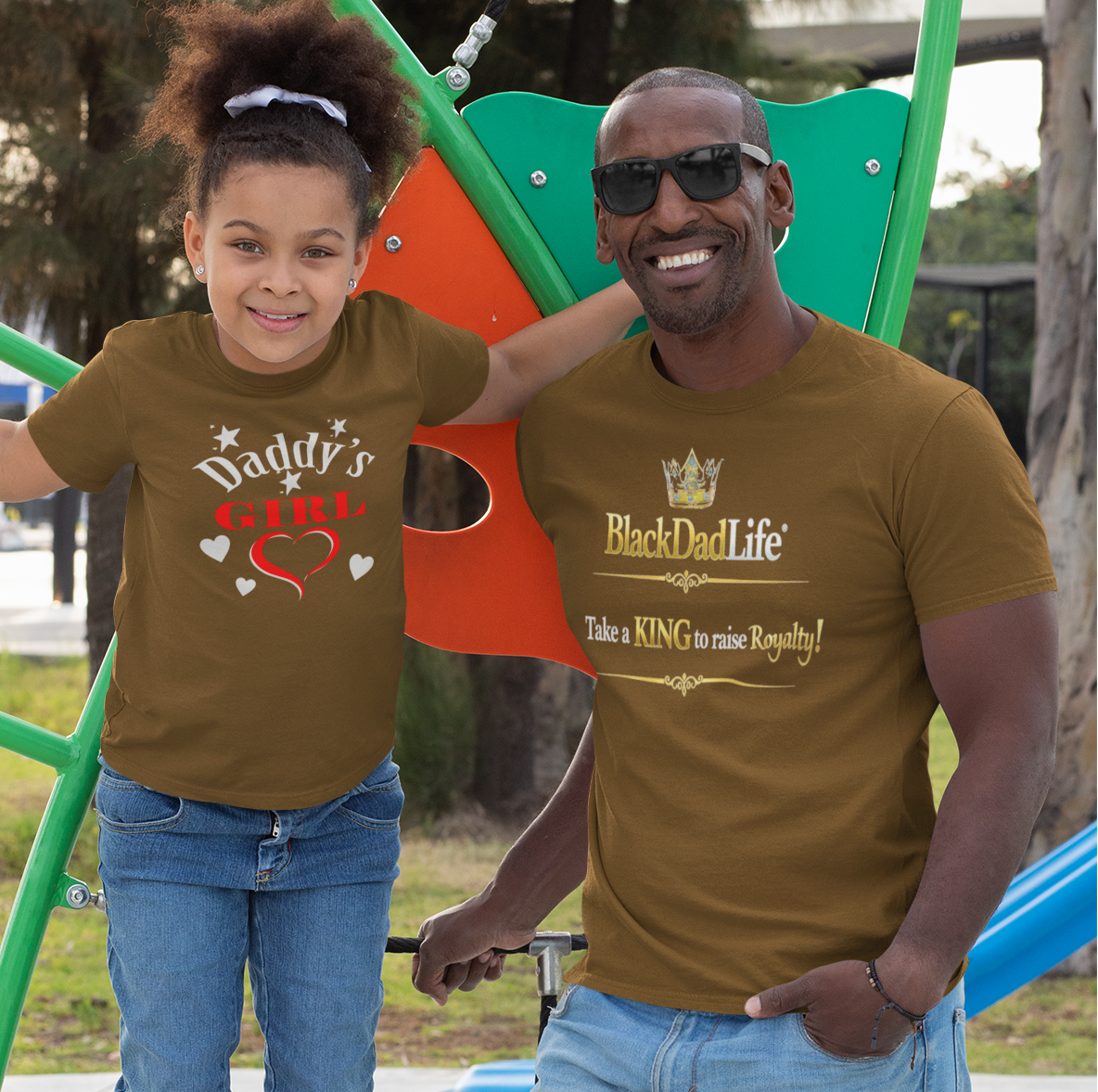 Man and young girl wearing matching 'Daddy's Little Queen' and 'BackDadLife' t-shirts outdoors.