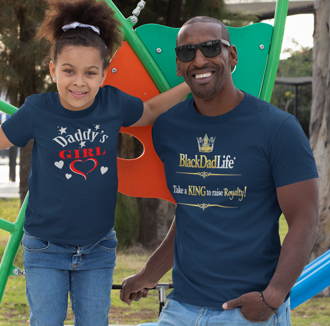 Man and young girl wearing matching blue t-shirts standing on a playground.