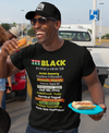 Man wearing a black t-shirt with colorful text, holding a hot dog and a plate, standing outdoors.