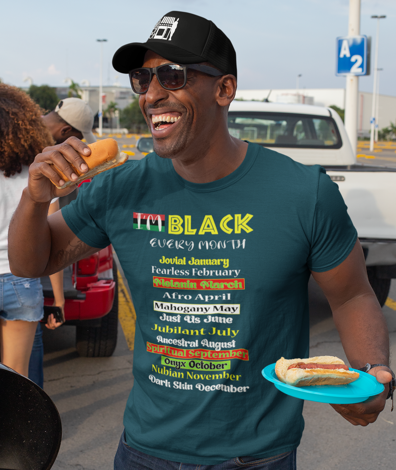 Man wearing a colorful t-shirt with text, holding a hot dog, and standing in an outdoor setting.