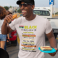 Man wearing a white t-shirt with 'Black History Month' text, holding hot dogs, and standing in a parking lot.