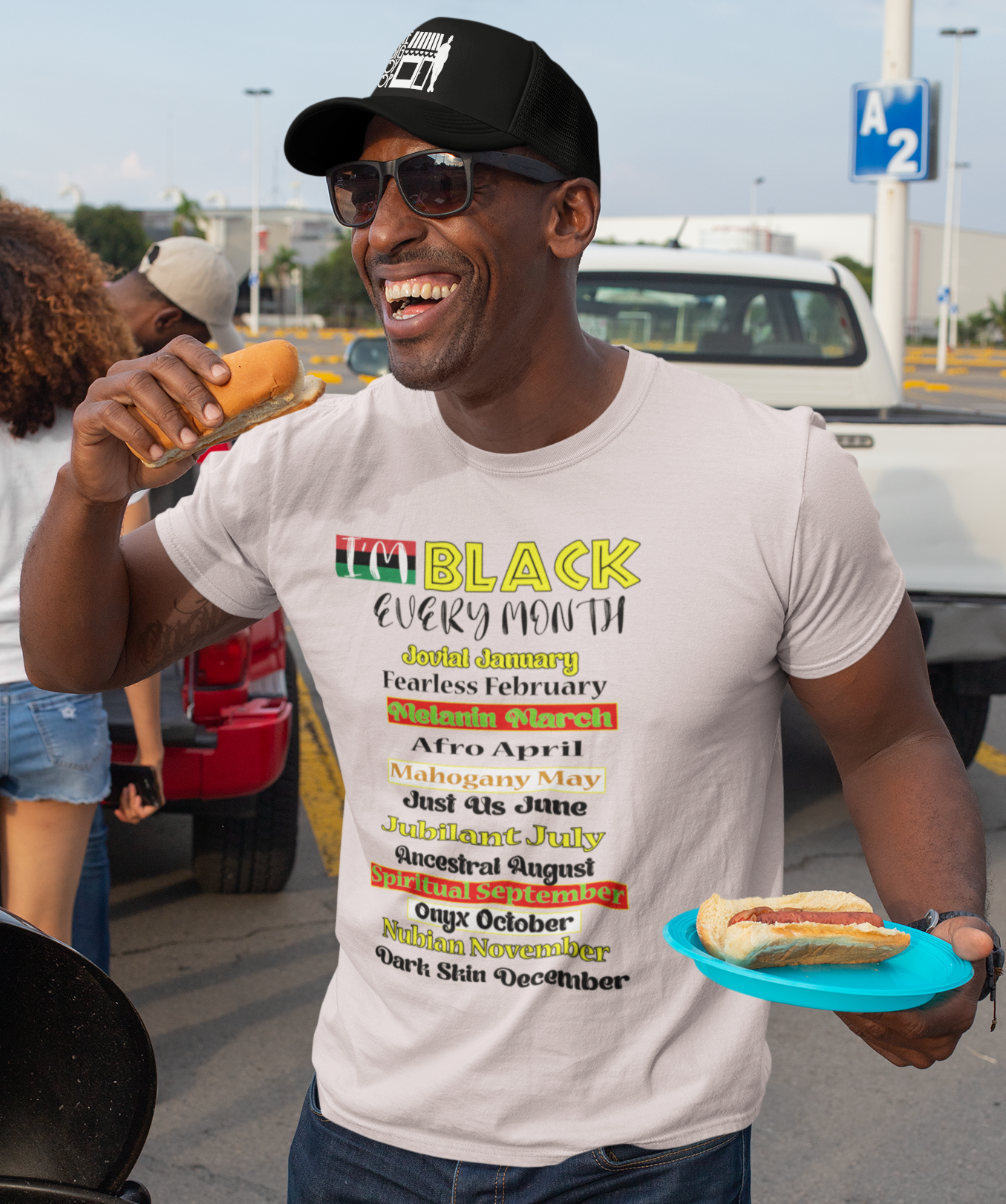 Man wearing a white t-shirt with 'Black History Month' text, holding hot dogs, and standing in a parking lot.