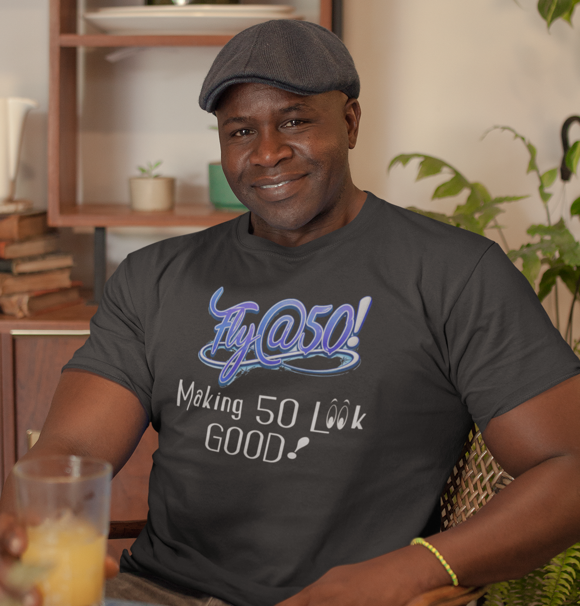 Man wearing a black t-shirt with text, holding a glass of orange juice in a home setting.