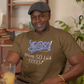 Man wearing a brown t-shirt with text, holding a glass of orange juice in a home setting.