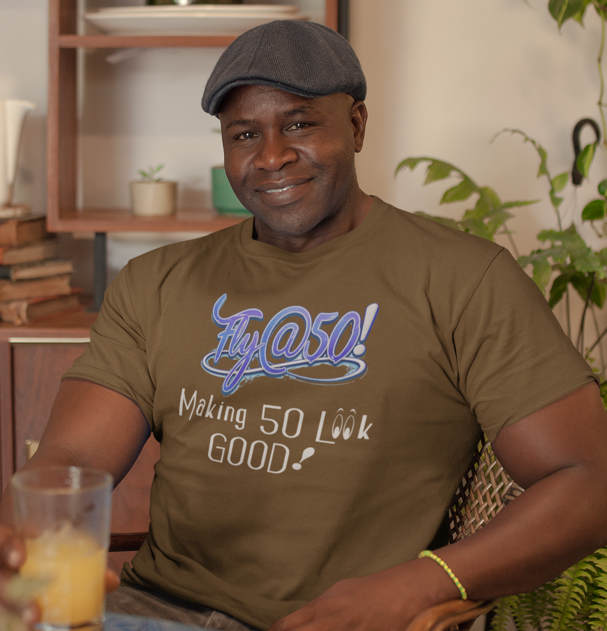 Man wearing a brown t-shirt with text, holding a glass of orange juice in a home setting.