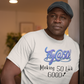 Man wearing a white t-shirt with 'Fly at 50! Making 50 Look Good!' text in a room.