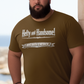Man wearing a navy blue t-shirt with text saying Hefty and Handsome with BIG Boy Energy underneath, standing by a stone wall with a scenic background.