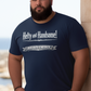 Man wearing a navy blue t-shirt with text saying Hefty and Handsome with BIG Boy Energy underneath, standing by a stone wall with a scenic background.