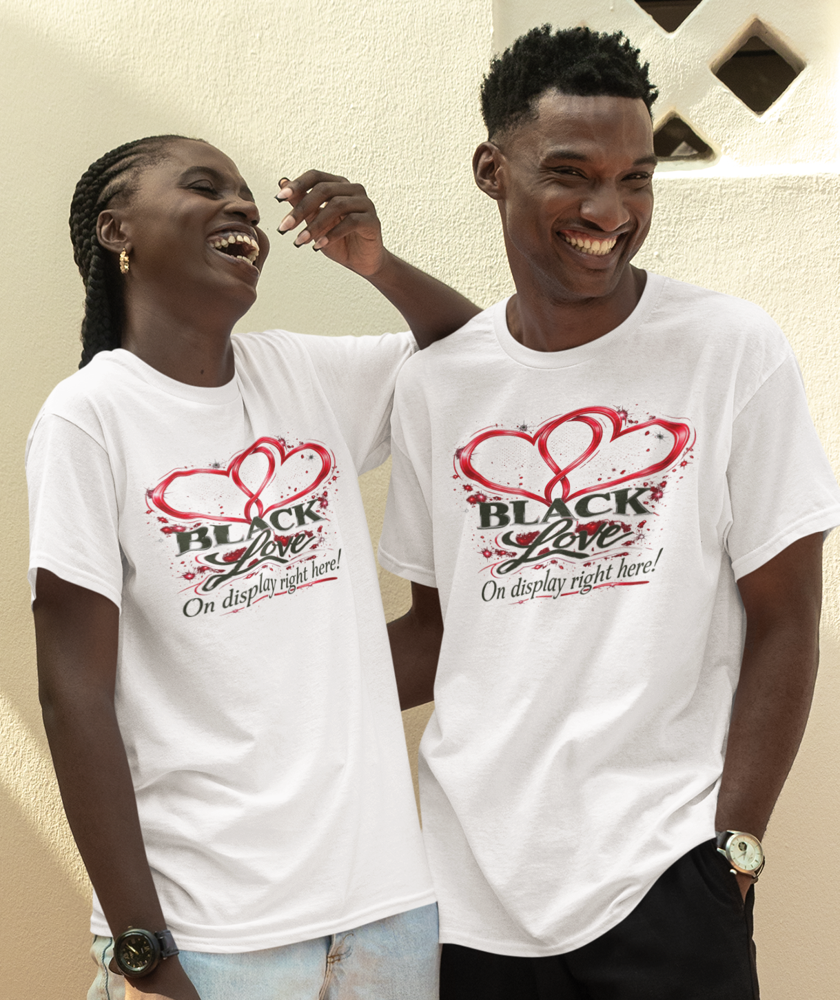 Two people wearing white t-shirts with a logo, standing outdoors against a beige wall.