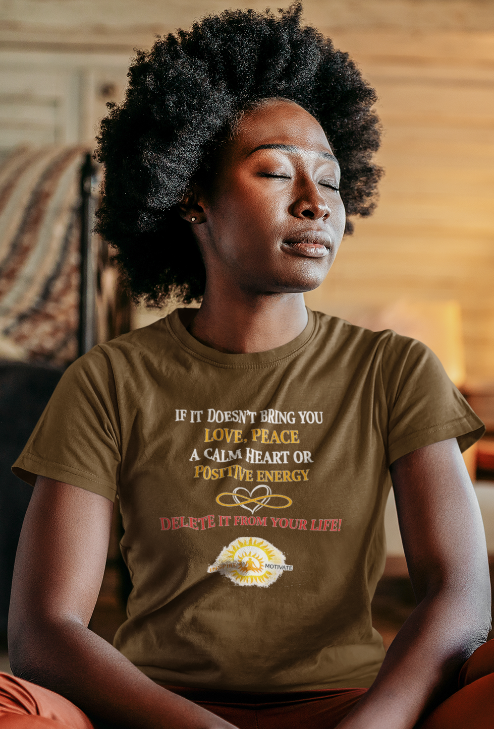 Woman meditating in a cozy room wearing a brown t-shirt with text.