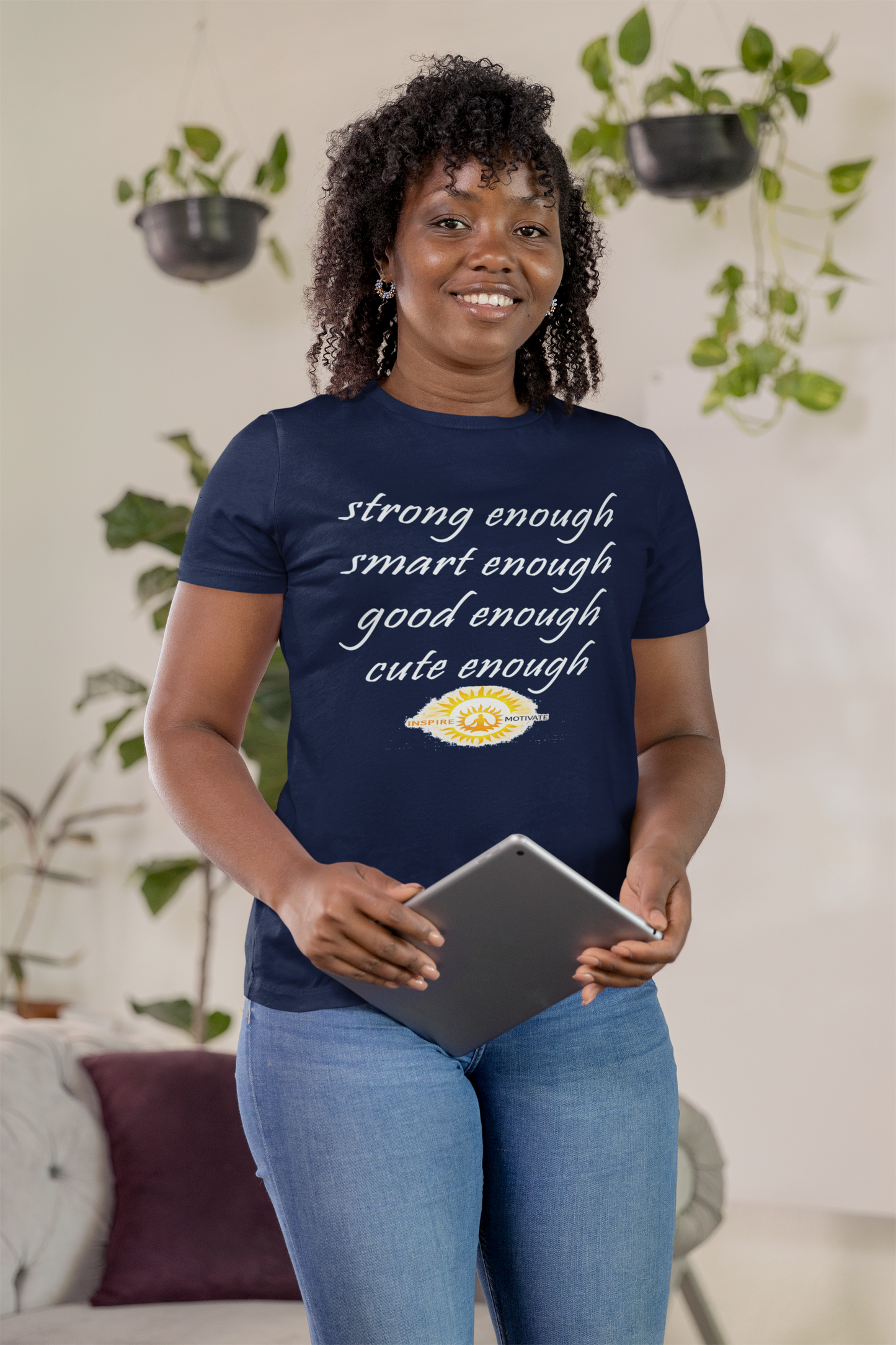 Woman wearing a navy blue t-shirt with text, holding a tablet, in a room with plants.