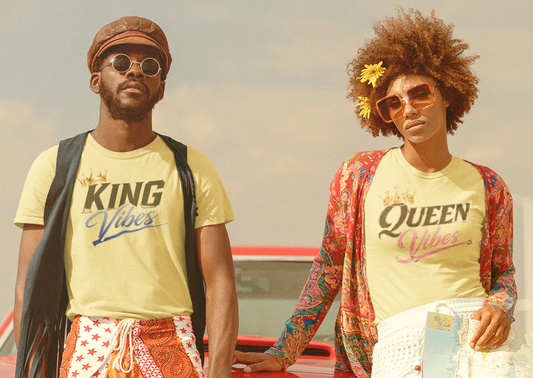 Two people standing in front of a vintage car with a suitcase, wearing matching t-shirts with 'KING' and 'QUEEN'.