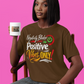 Person wearing a brown t-shirt with a motivational quote, holding a mug against a pink background