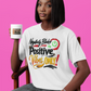 Person wearing a white t-shirt with colorful text and holding a mug against a pink background