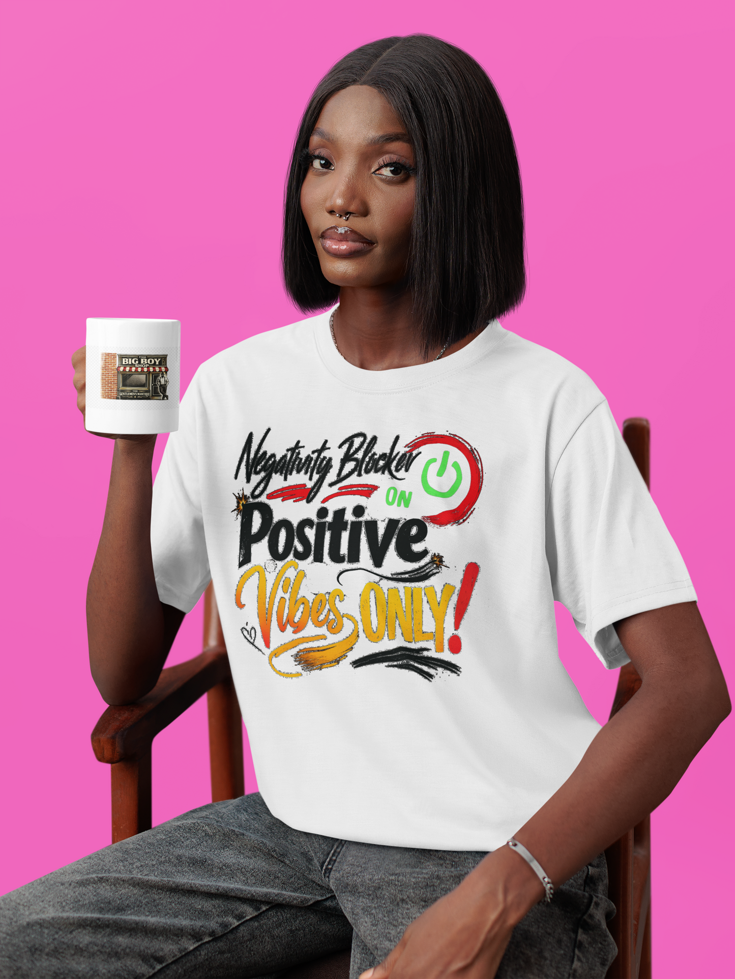 Person wearing a white t-shirt with colorful text and holding a mug against a pink background